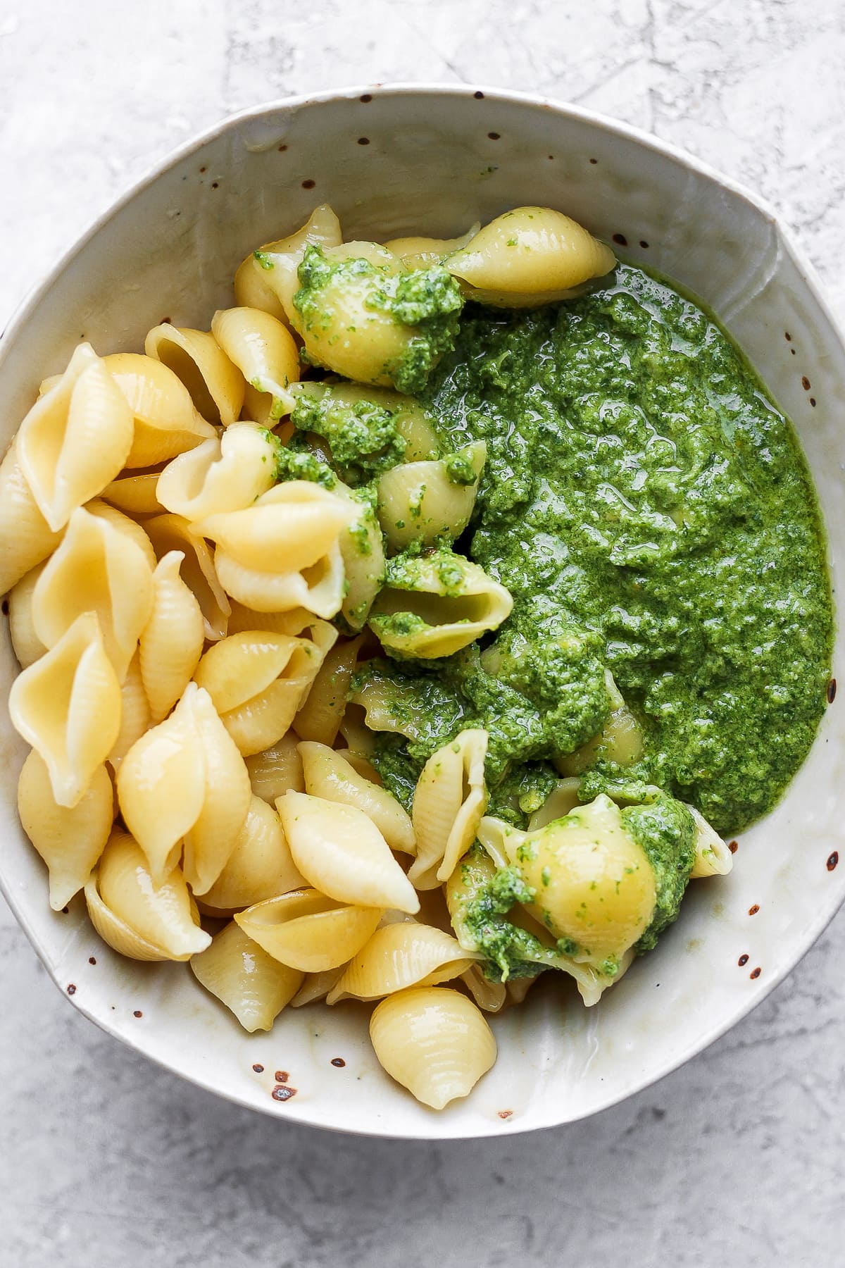 Bowl of cooked pasta shells and vegan pesto. 