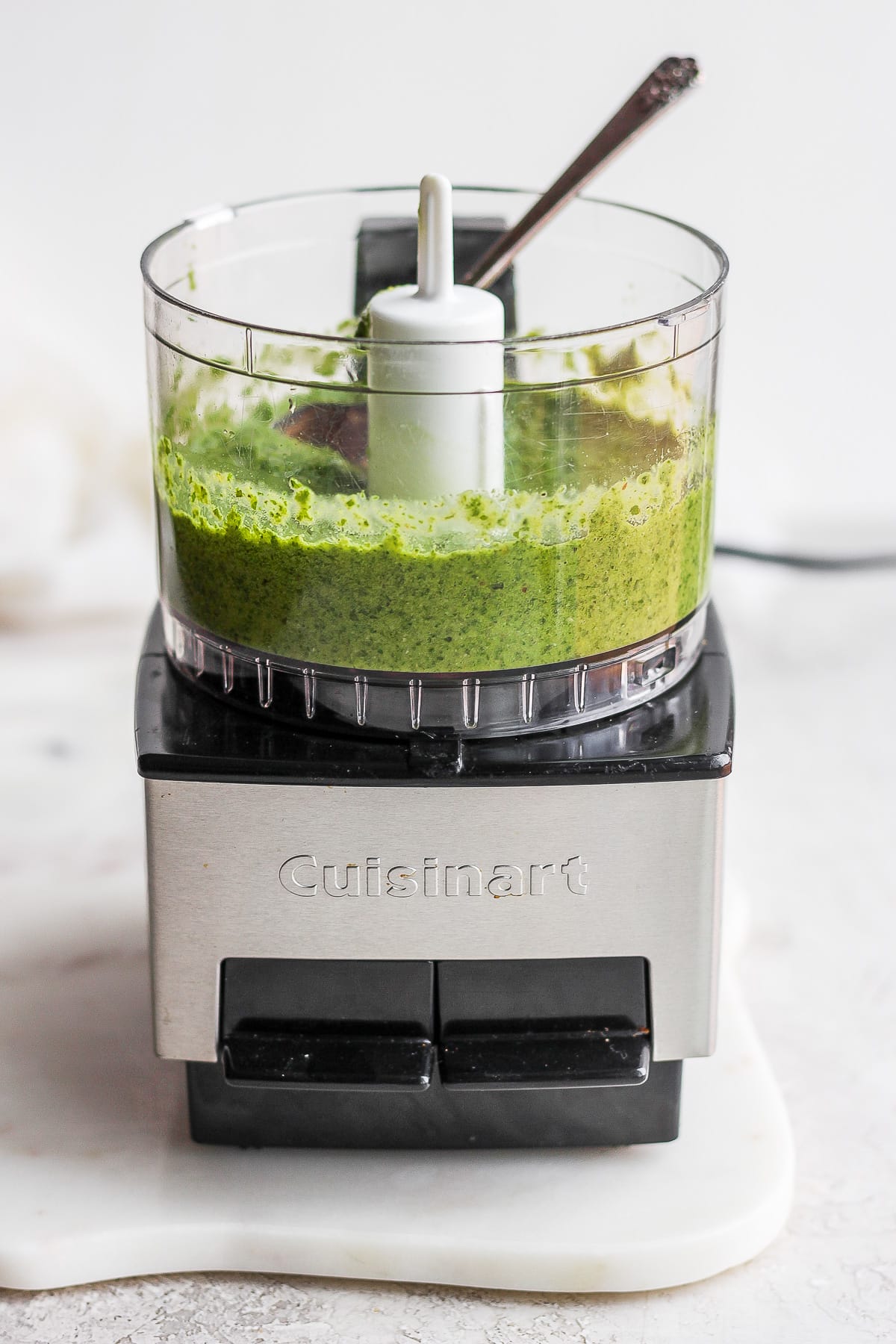 Small food processor with homemade dairy-free pesto inside and a spoon sticking out. 