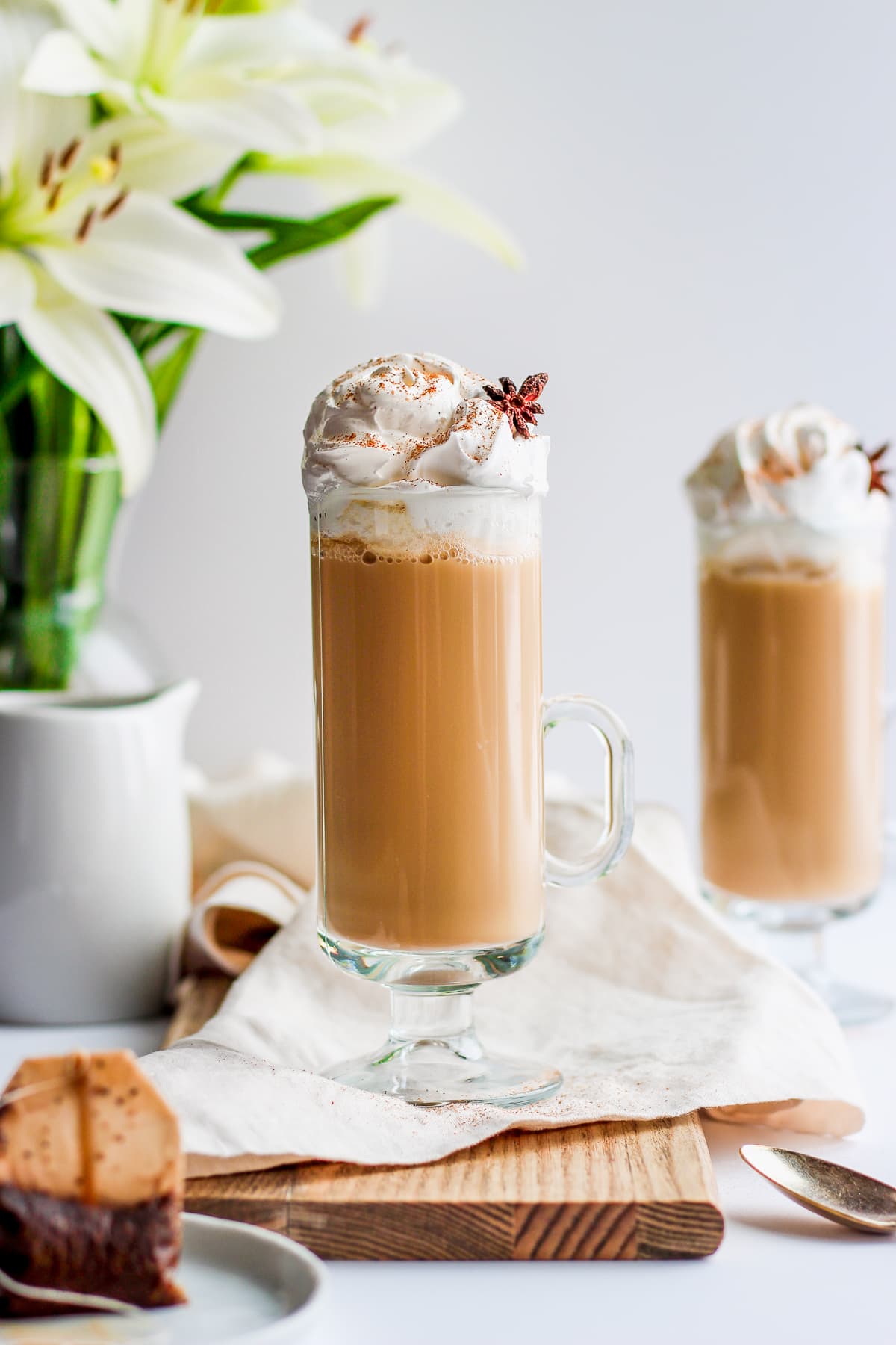 Glass of chai tea latte on a wooden board with flowers in the background.