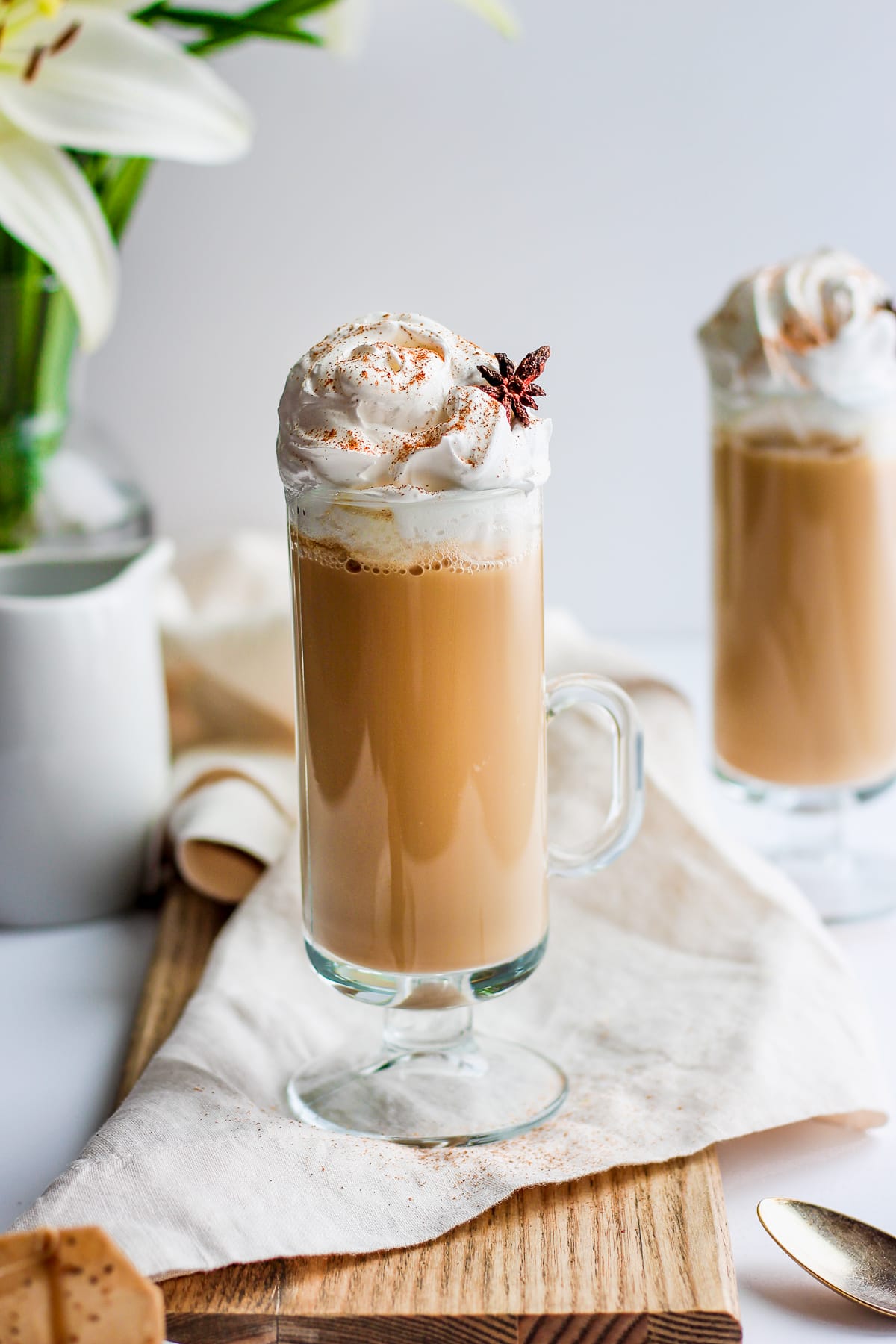 Glass of chai tea latte on a wooden board with flowers in the background.