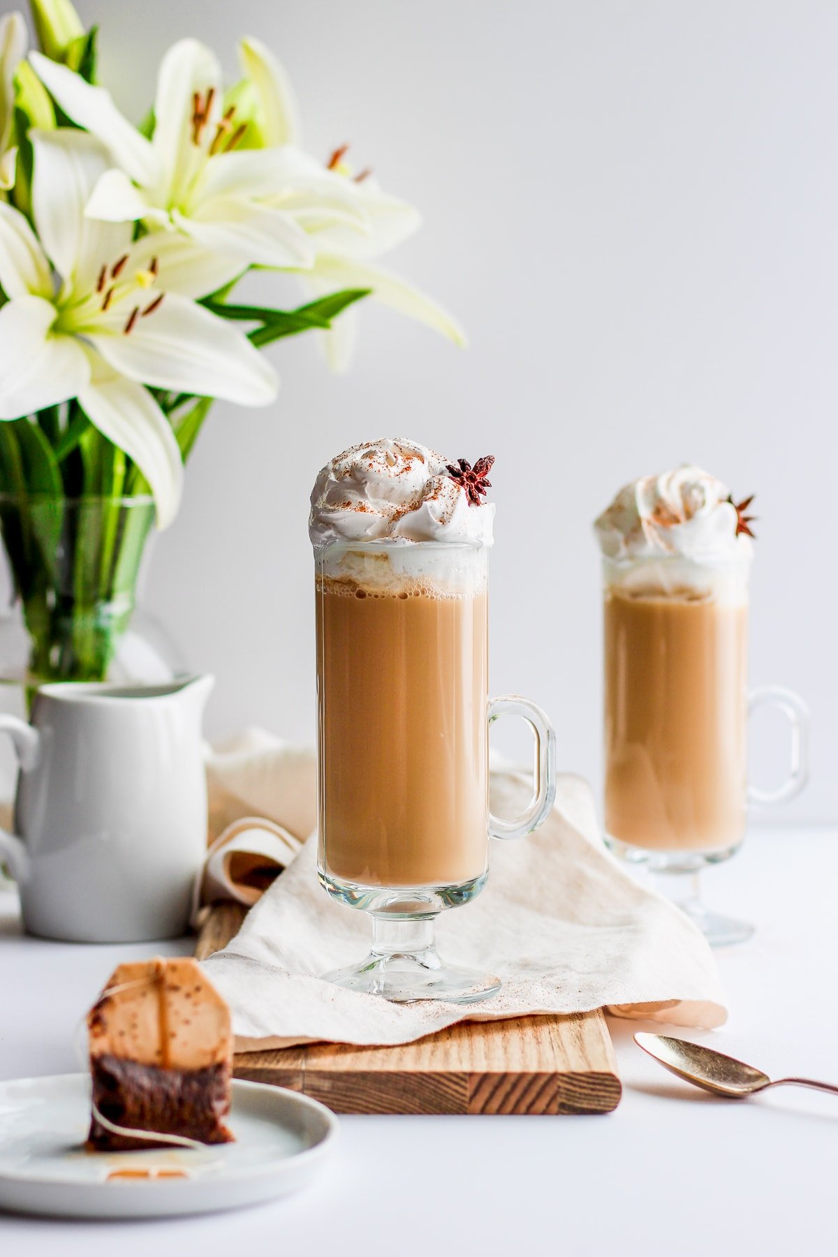 Glass of chai tea latte on a wooden board with flowers in the background.