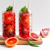 Two glasses of blood orange spritzer with straws and garnished with fresh mint.