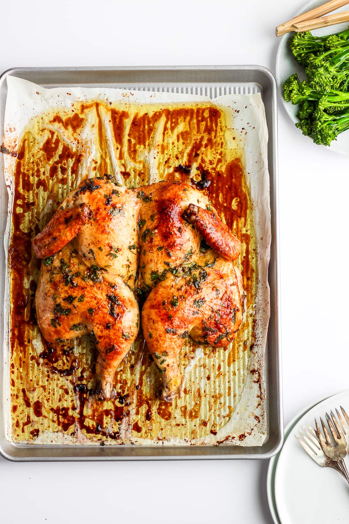 Farther away shot of a roasted spatchcock chicken on a parchment lined baking sheet.