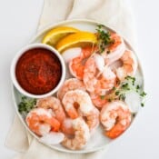 A white plate full of shrimp cocktail and shrimp cocktail sauce in a small dish.