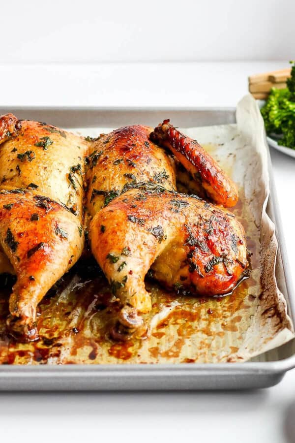 Side view of a spatchcock chicken on a parchment-lined baking sheet.