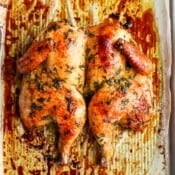 A whole roasted spatchcock chicken on a parchment-lined baking sheet.