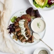A small dish of horseradish sauce on a plate with sliced steak, also drizzled in sauce, and a spoon.