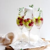 Three champagne glasses of frozen grape mimosa mocktails with fresh thyme for garnish.