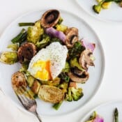 Roasted veggies on a white plate with a poached egg on top and a fork on the side.