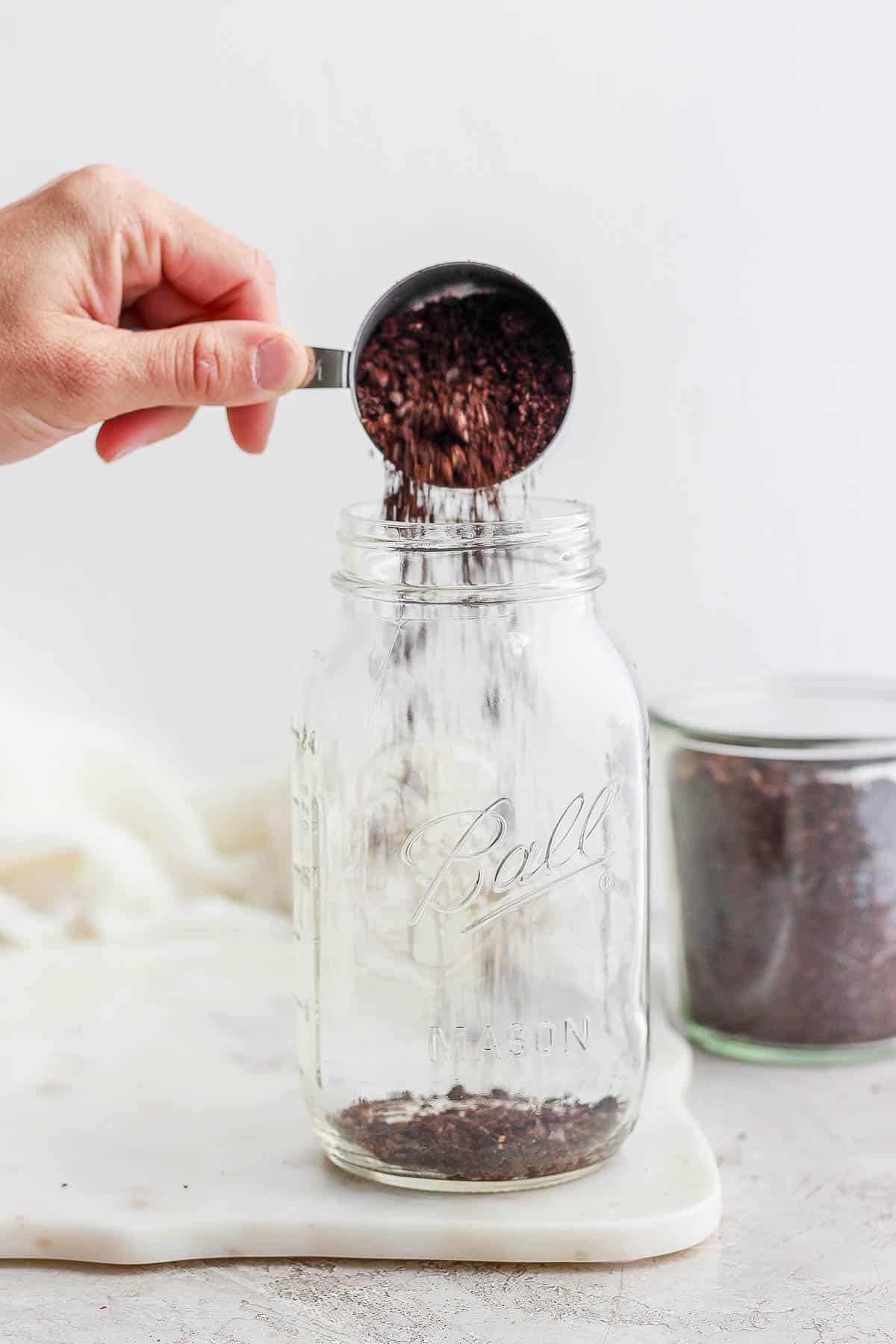Someone pouring roughly ground coffee beans into a large mason jar. 