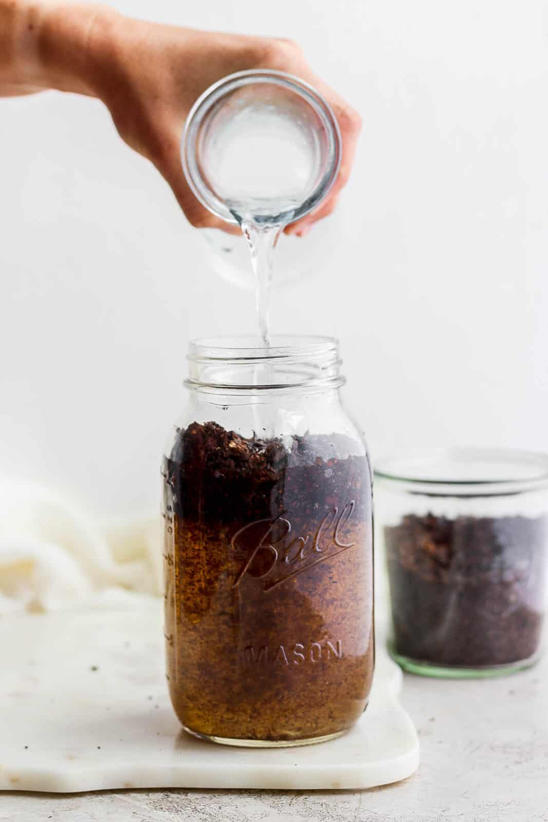 Someone adding water to the roughly ground coffee beans inside the mason jar. 