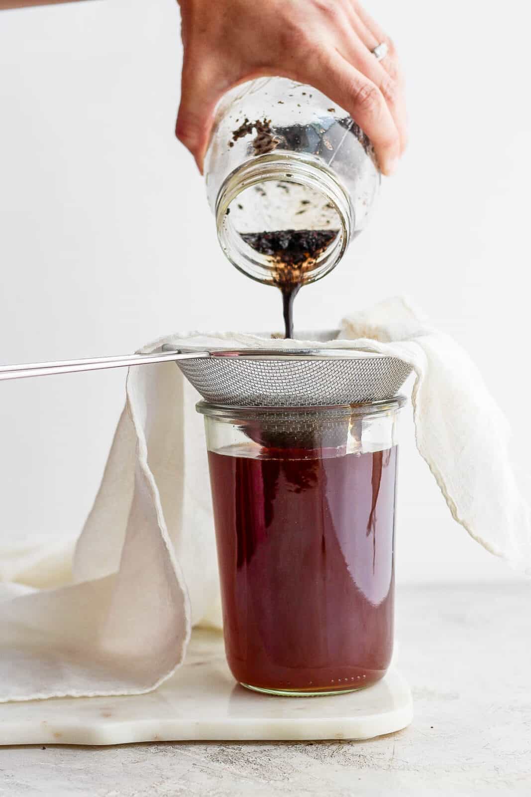 Someone pouring out cold brew coffee and coffee beans and through a cheesecloth to strain out the coffee beans. 