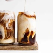 Two glasses of cold brew with creamer being poured into one of the glasses.