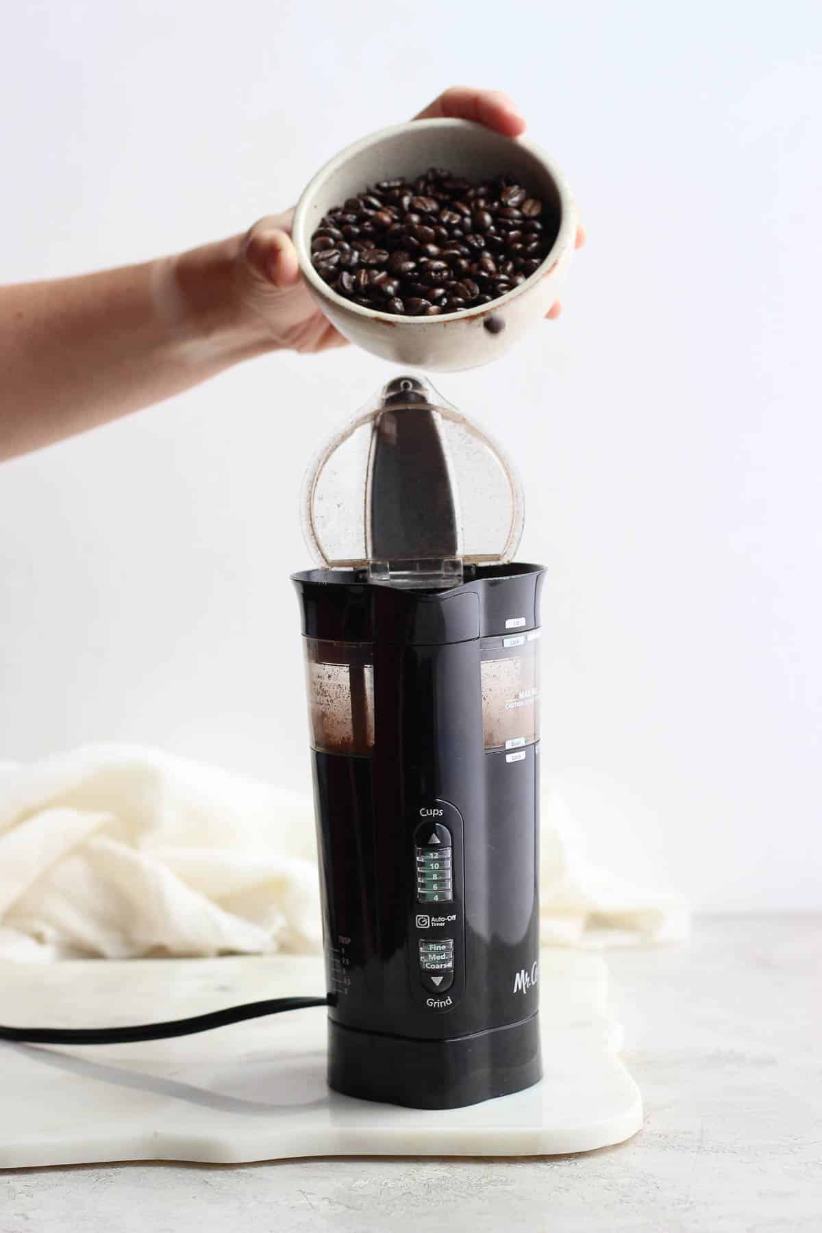 Someone pouring whole coffee beans into a coffee grinder. 