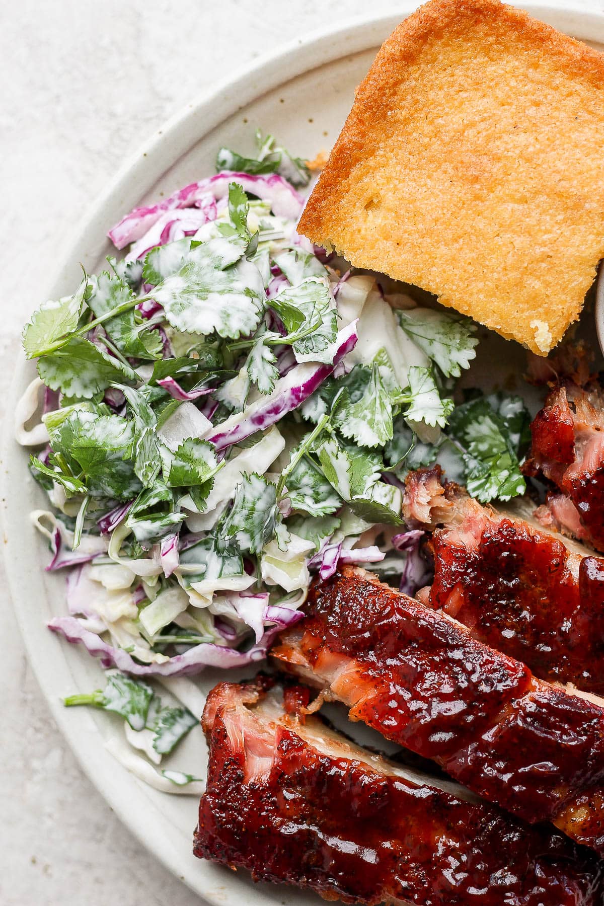 Plate of smoked ribs, gluten-free cornbread and spicy purple cabbage coleslaw. 