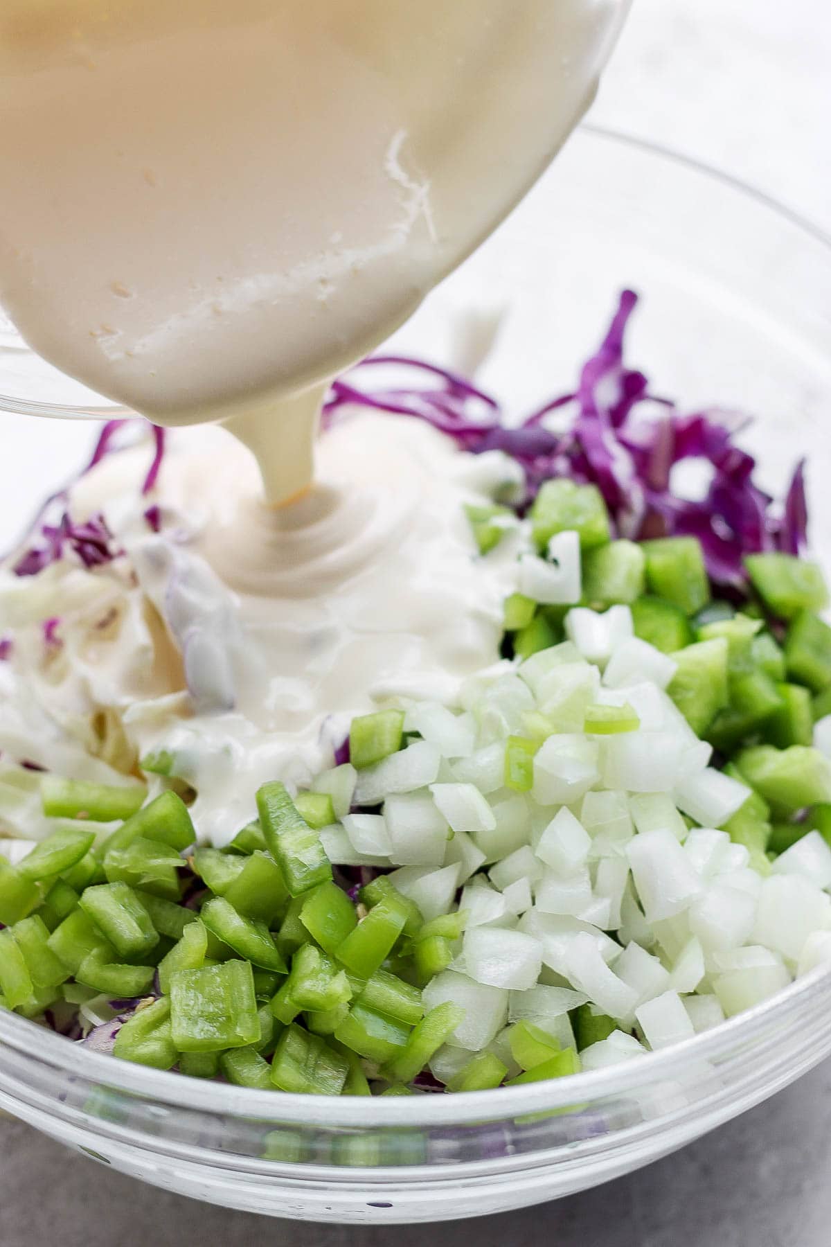 Bowl of coleslaw ingredients with dressing being poured inside. 