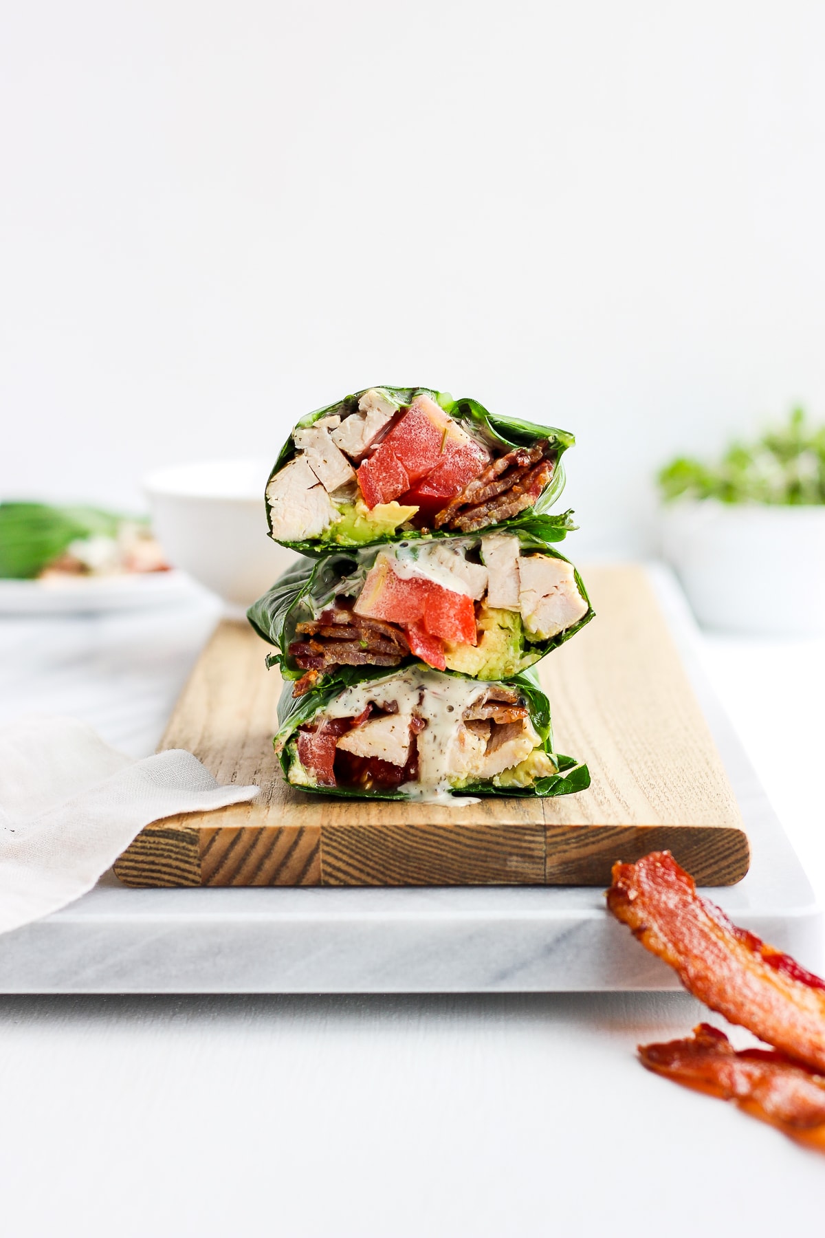 Chicken bacon club collard green wraps stacked on a cutting board.