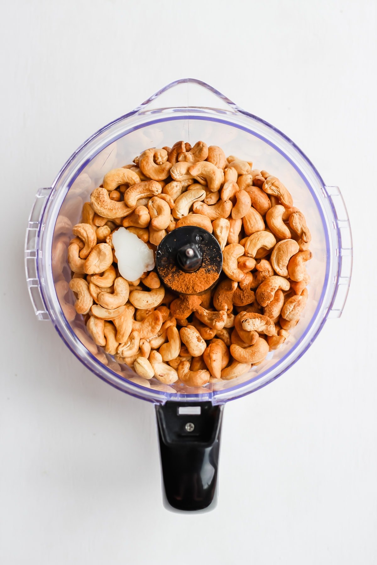 Top shot of a food processor with ingredients inside for cashew butter.