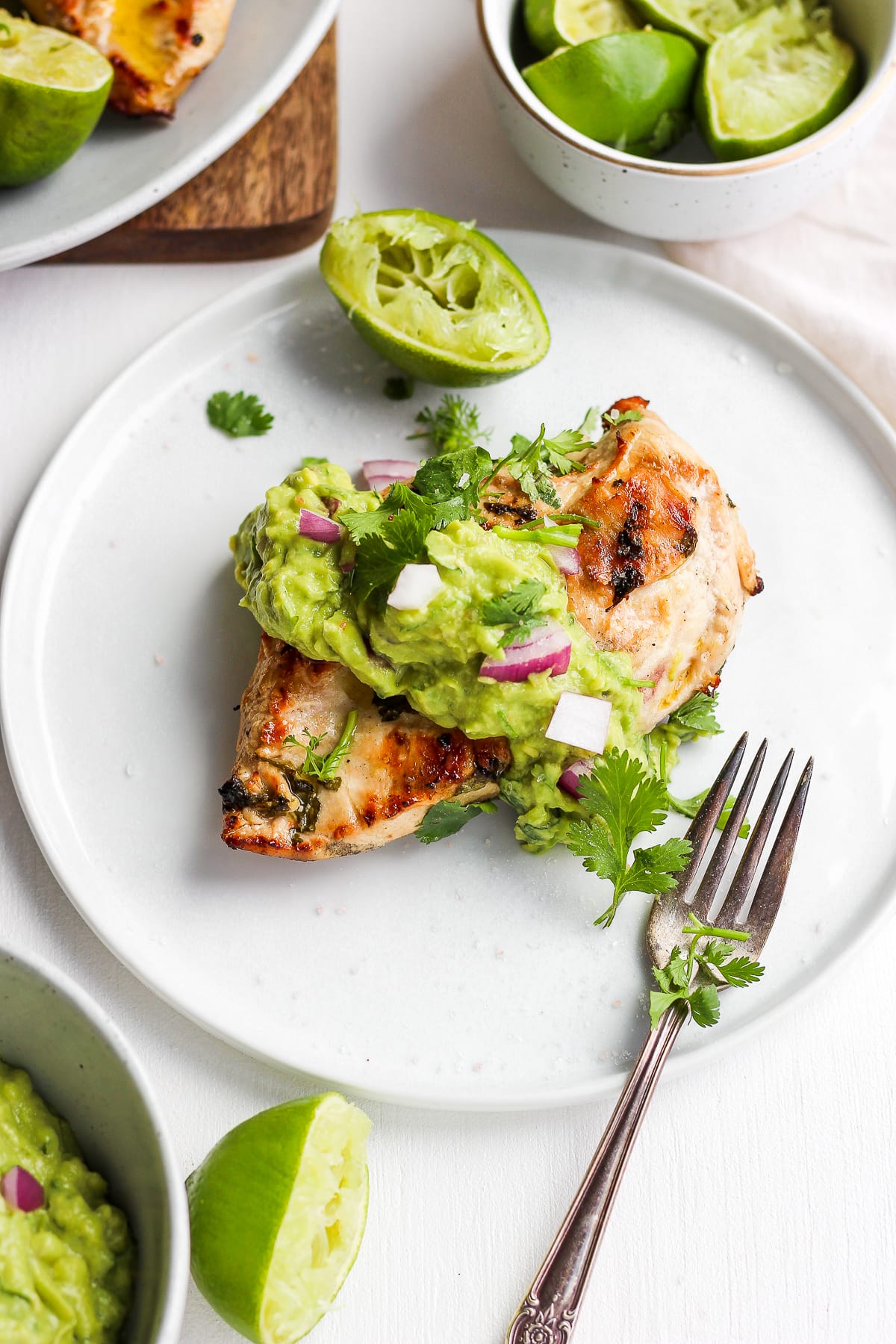 Plate of grilled cilantro lime chicken with guacamole on top and fresh limes. 