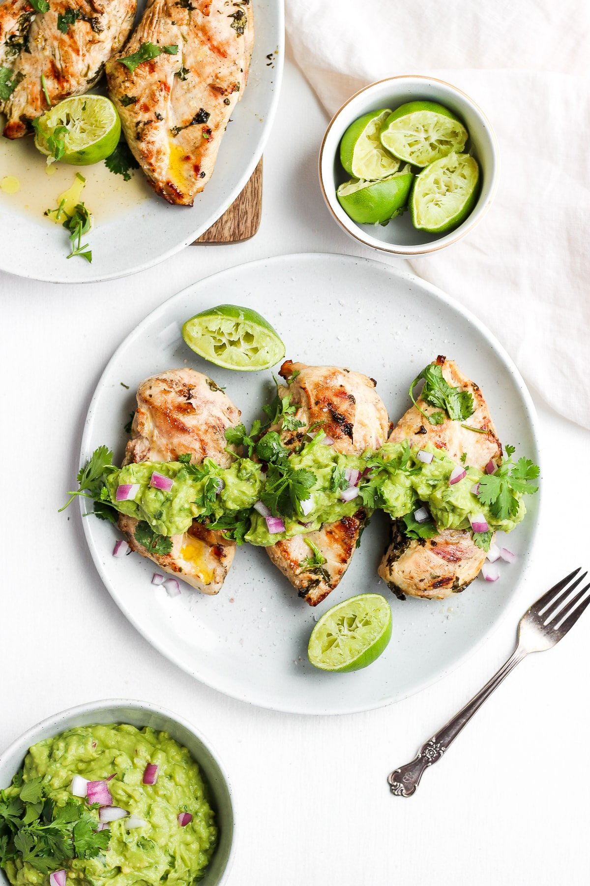 Plate of grilled cilantro lime chicken with guacamole on top and fresh limes. 
