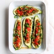 A white baking dish full of four halves of stuffed zucchini.