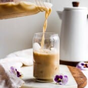 A glass of iced cold brew bulletproof being poured with a kettle in the background.