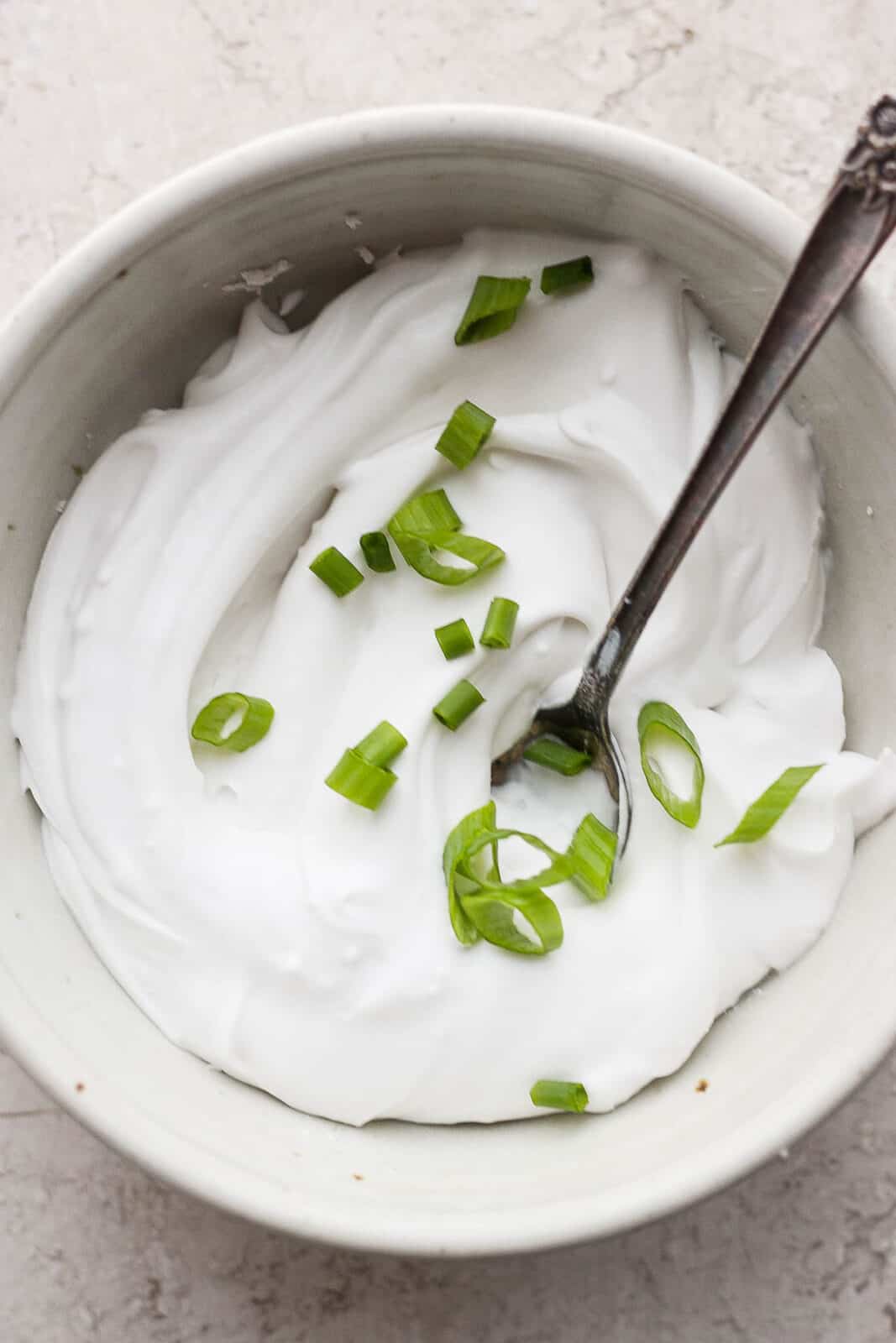 A bowl of dairy free sour cream with green onions on top.