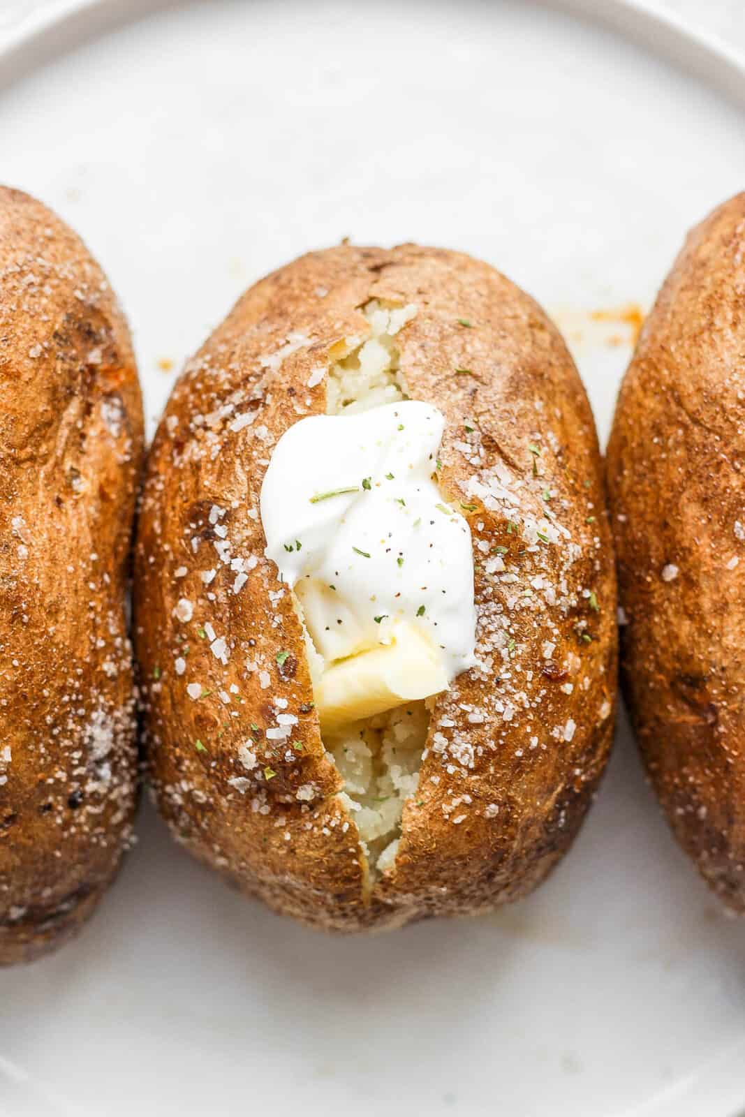 Three baked potatoes with the middle one having dairy free sour cream on it. 