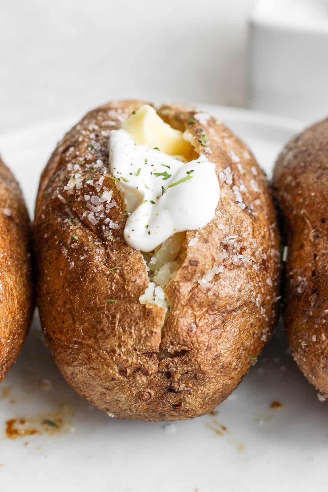 Three baked potatoes with the middle one having dairy free sour cream on top. 