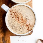 A mug of cinnamon cold brew cashew latte on a cutting board with a spoon off to the side.