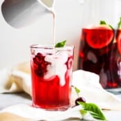 A glass of hibiscus iced tea cooler with a non-dairy creamer being poured in.