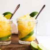 Two glasses of granita on a wood cutting board with lime wedges for garnish.