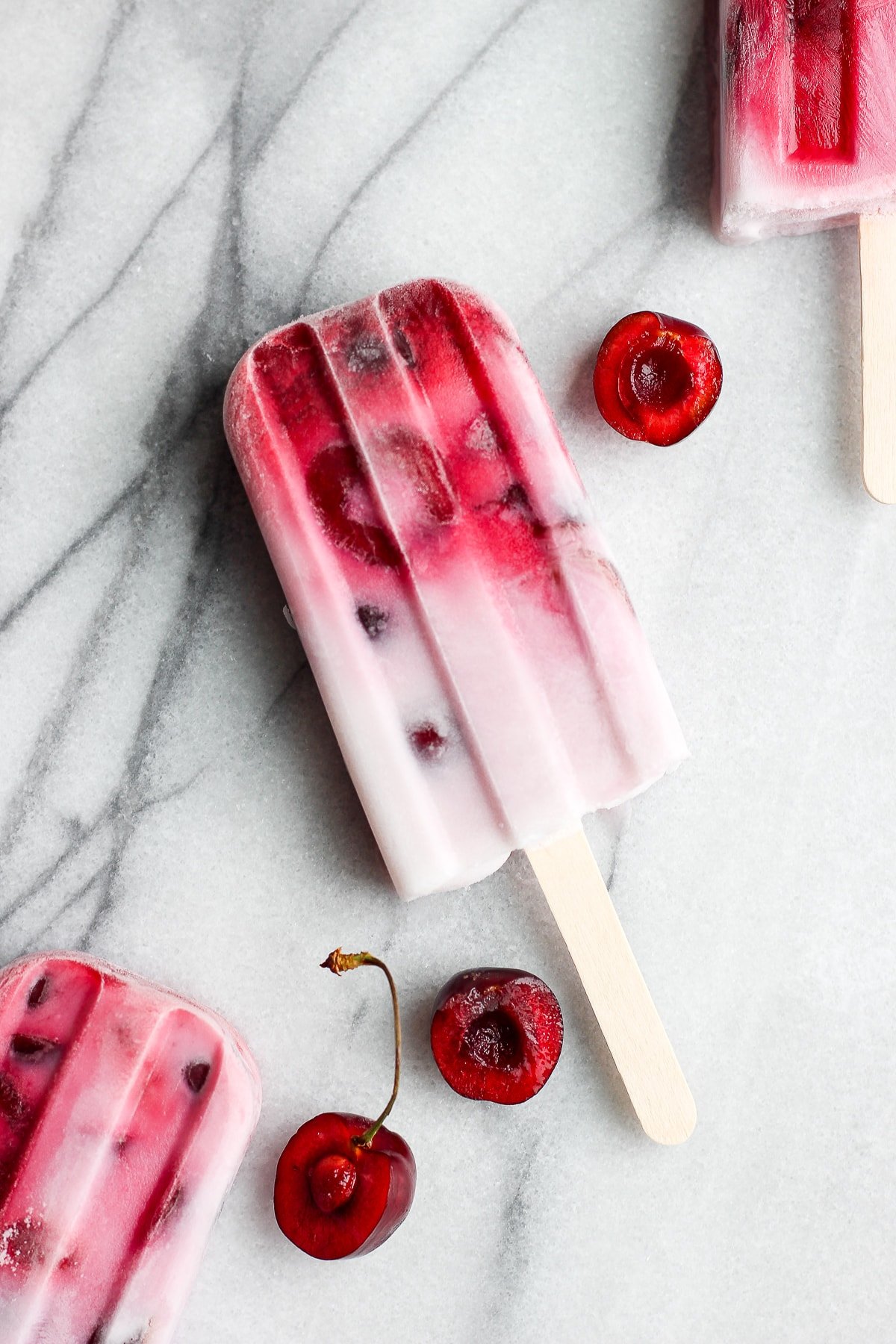 A strawberry cherry and cream popsicle with some fresh cherries.