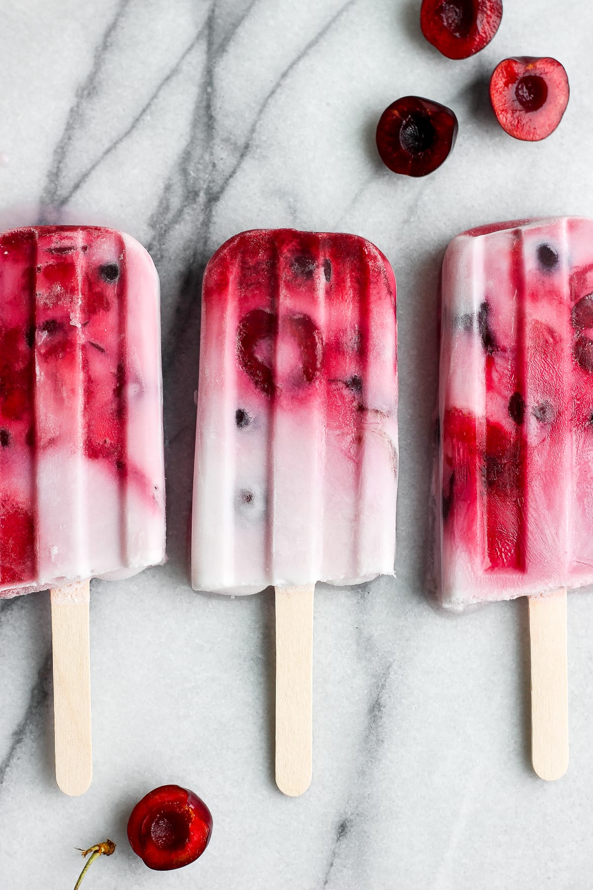 Three strawberry cherry and cream popsicles on the counter.