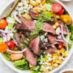 A big bowl of flank steak salad with corn, tomatoes and chimichurri sauce.