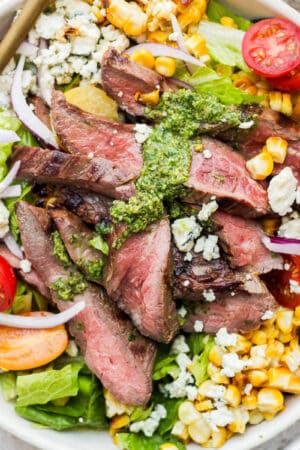 A big bowl of flank steak salad with corn, tomatoes and chimichurri sauce.