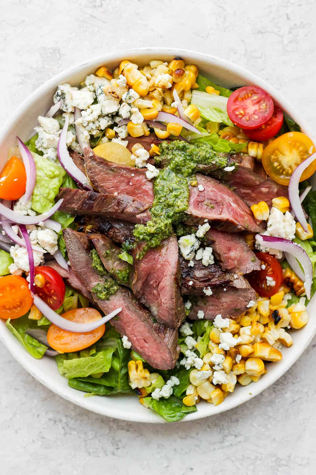 Bowl of flank steak salad with blue cheese, tomatoes and corn.