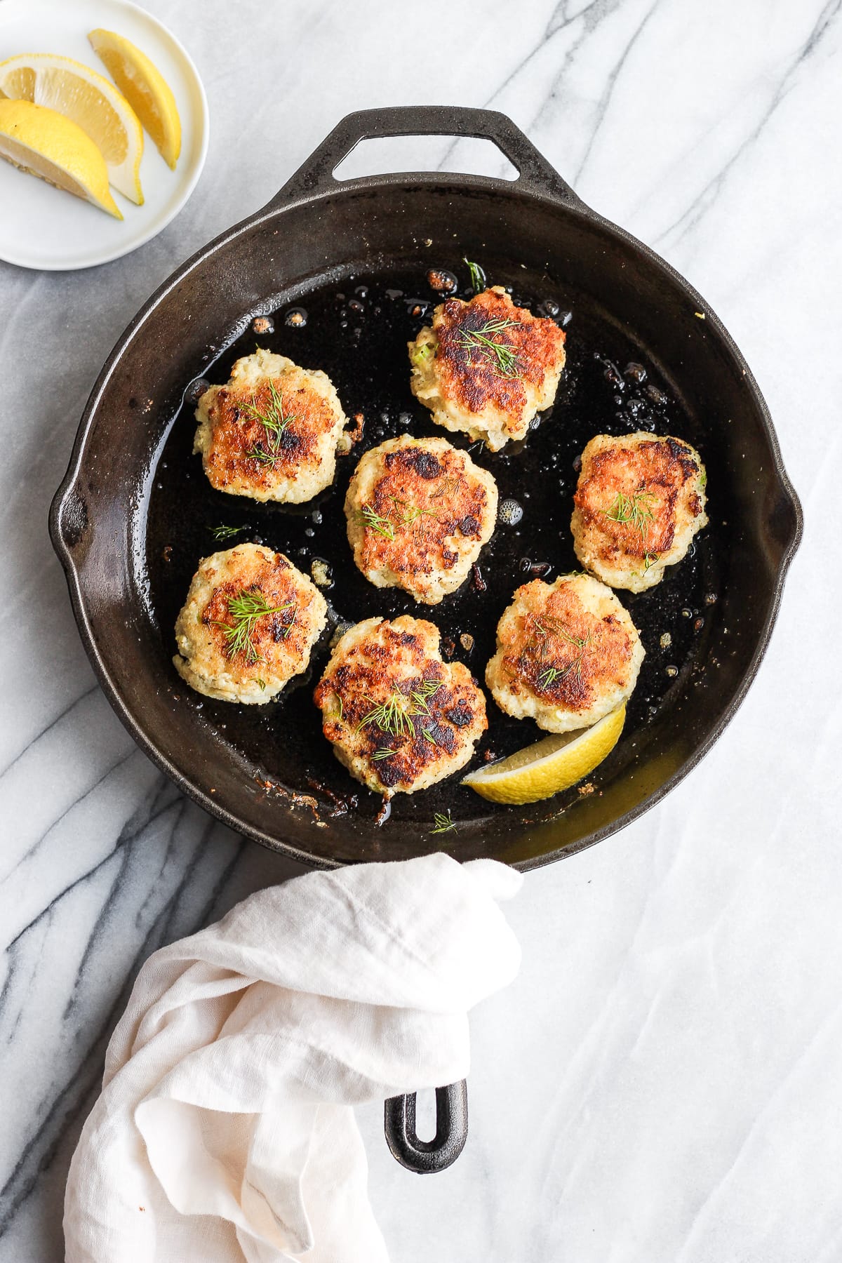 Cod cakes searing in a large cast iron skillet.