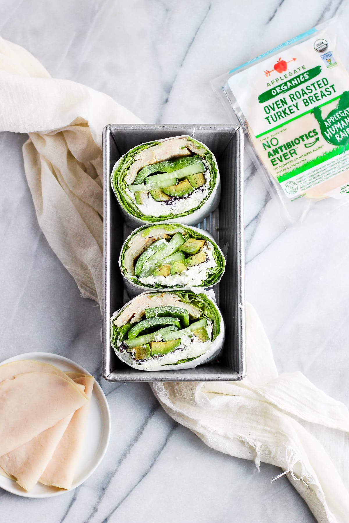 Halves of a turkey lettuce wrap in a metal pan next to a package of Applegate turkey deli meat.