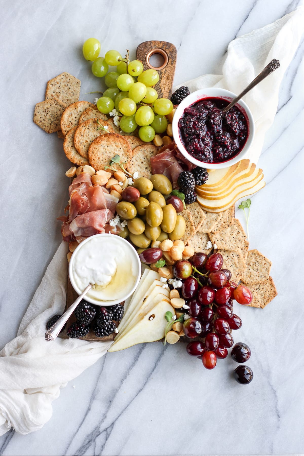 A charcuterie board with grapes, olives, spreads, meats, and cheeses.
