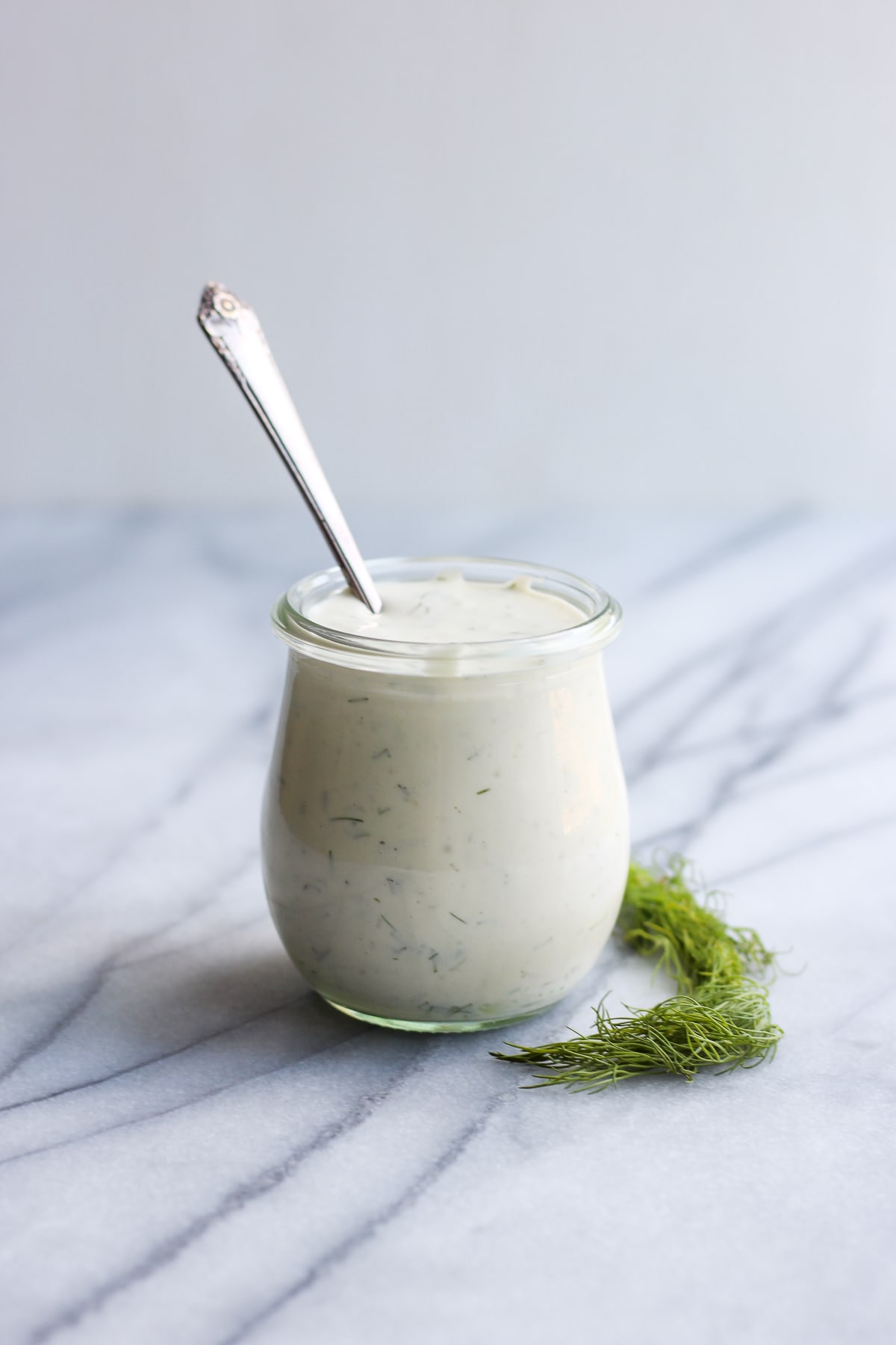Tartar sauce in a glass jar on a counter top with a spoon sticking out of the jar.