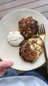 Someone holding a plate of cod fish cakes with a dollop of tartar sauce next to them.