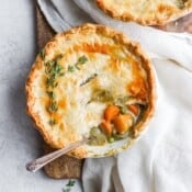 A Fall harvest pot pie on a wooden board with a spoon in the side of the bowl.