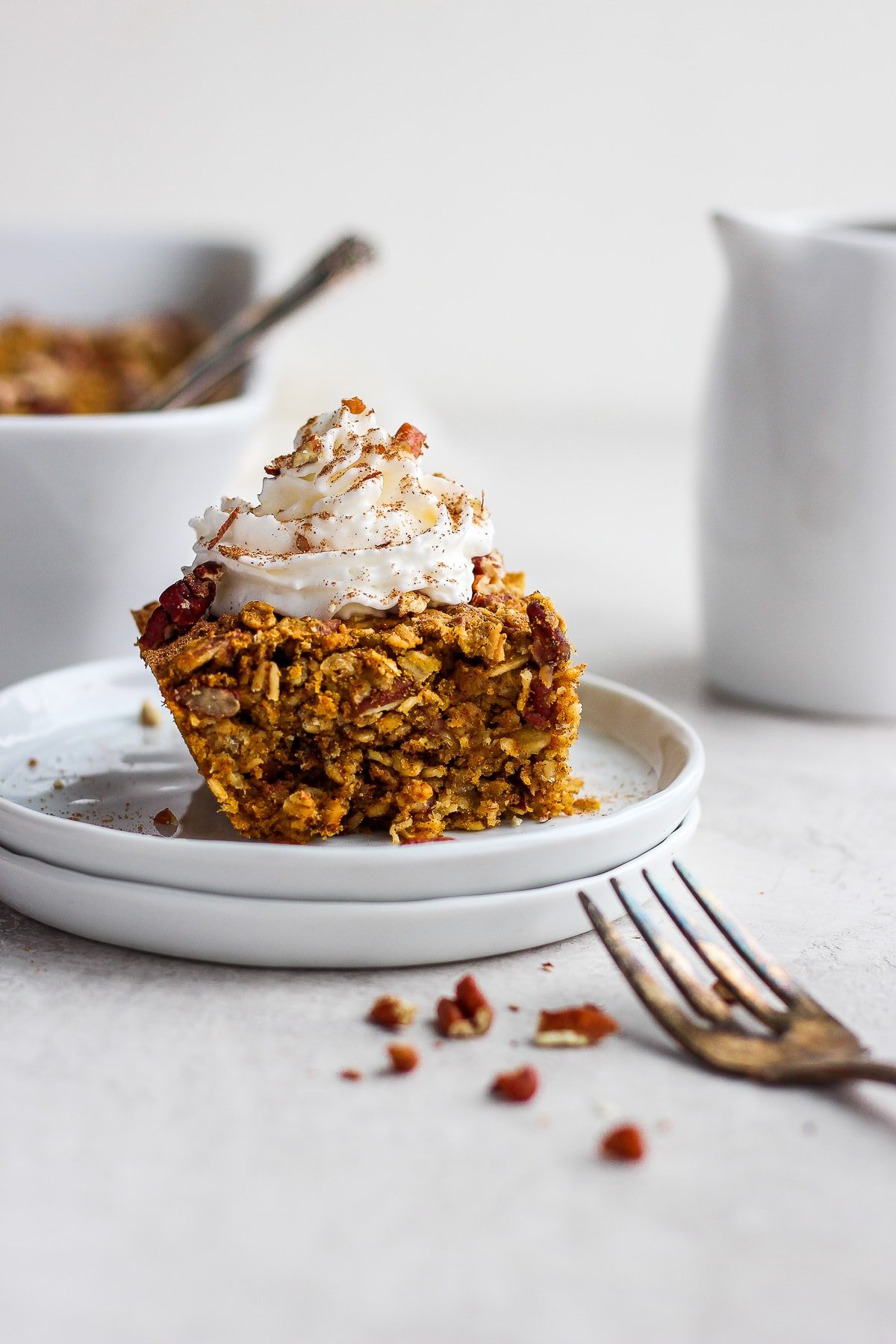 A slice of pumpkin oatmeal bake on a white plate with whipped cream on top.