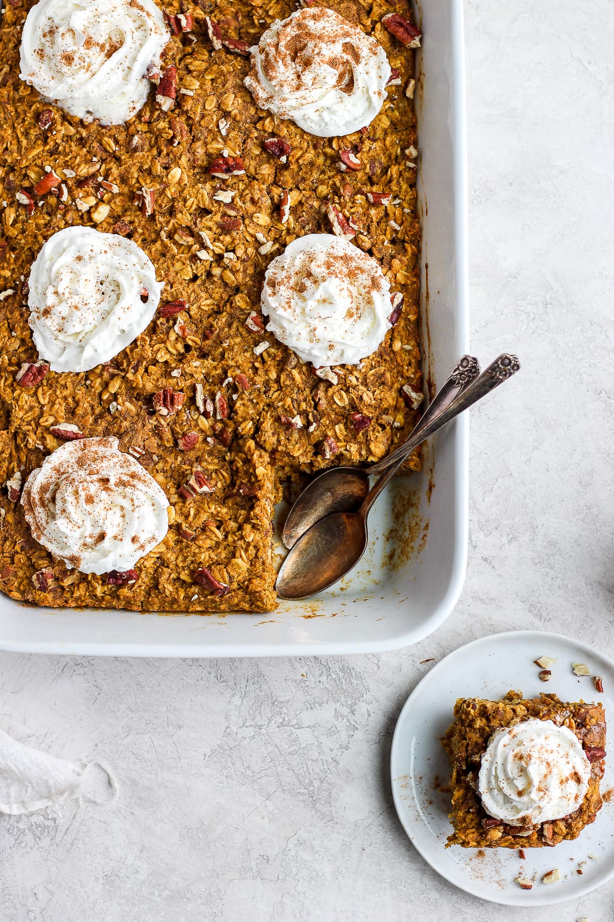 Pumpkin baked oatmeal in a white baking dish with one serving removed and placed on a plate.