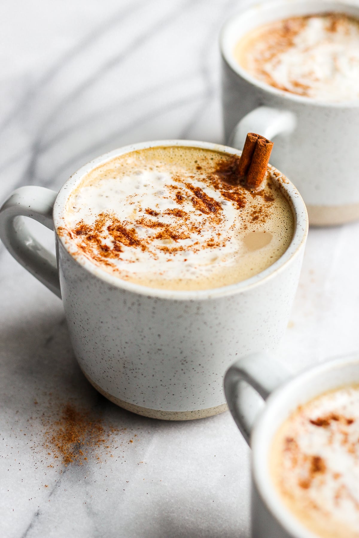 Side view of a mug of pumpkin spice latte with a cinnamon stick popping out. 