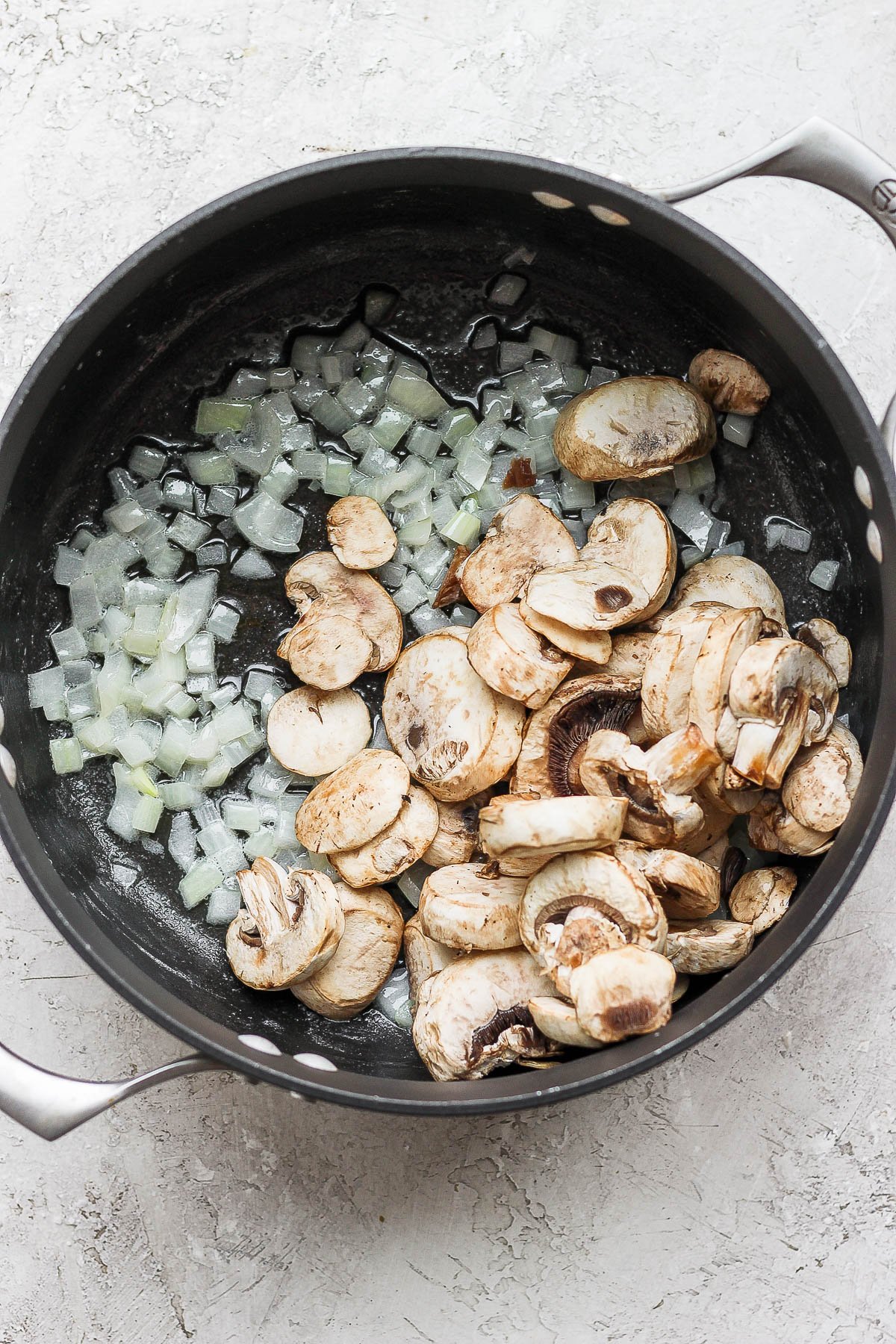 A pot with onion and mushrooms sautéing.
