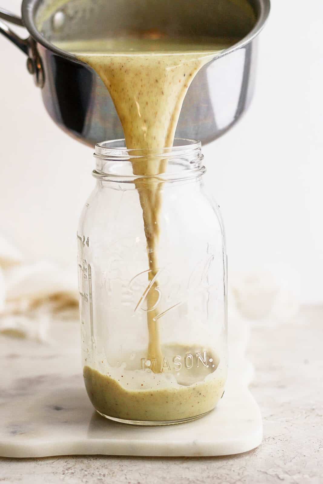 Someone pouring dairy free egg nog into a large mason jar. 