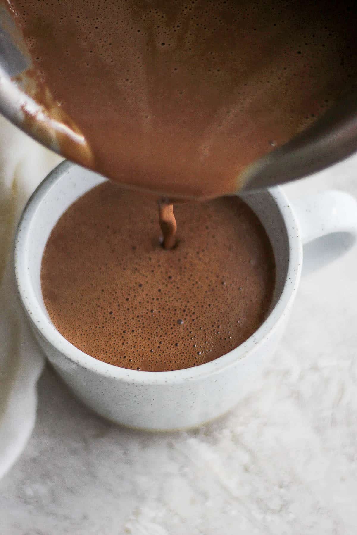 Top shot of someone pouring dairy-free hot chocolate into mug.