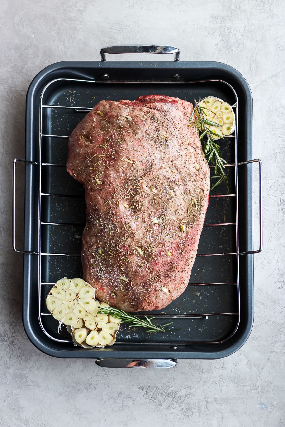 Ultimate Leg of Lamb sitting in a roasting pan covered in lamb seasoning.